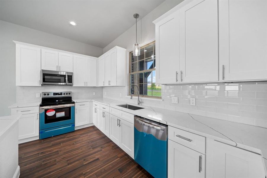 Kitchen with dark wood-type flooring, stainless steel appliances, light stone countertops, hanging light fixtures, and sink