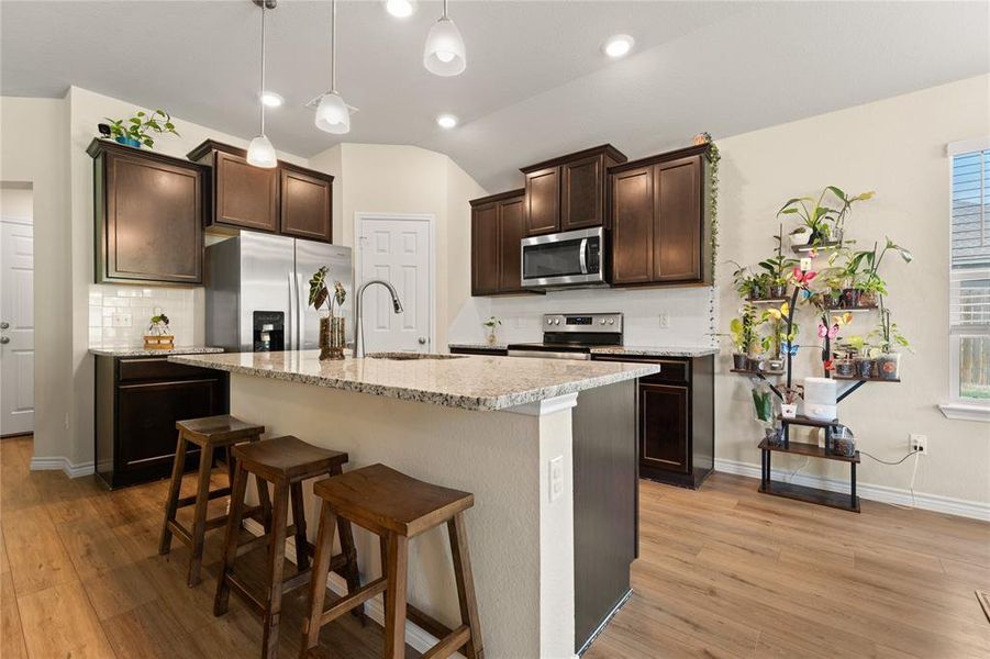 Kitchen featuring backsplash, dark brown cabinets, appliances with stainless steel finishes, a breakfast bar area, and light wood-style flooring