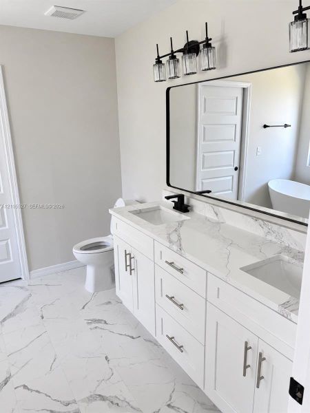 Dual vanity with white cabinetry and integrated sinks, complemented by a large framed mirror and a four-light fixture Dual vanity with white cabinetry and integrated sinks, complemented by a large framed mirror and a four-light fixture