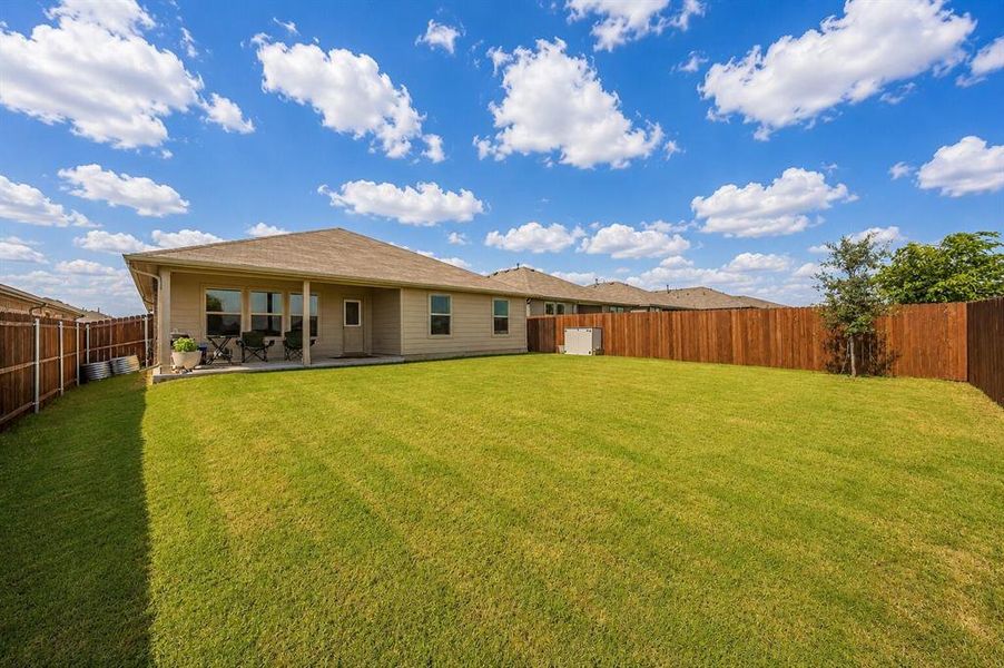 Expansive backyard featuring a lush lawn, privacy fencing, and a covered concrete patio