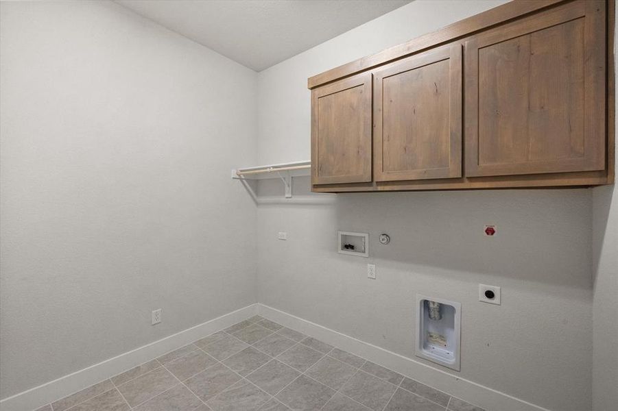Separate laundry room has room for a freezer and features tile flooring, cabinet space and hanging rod.