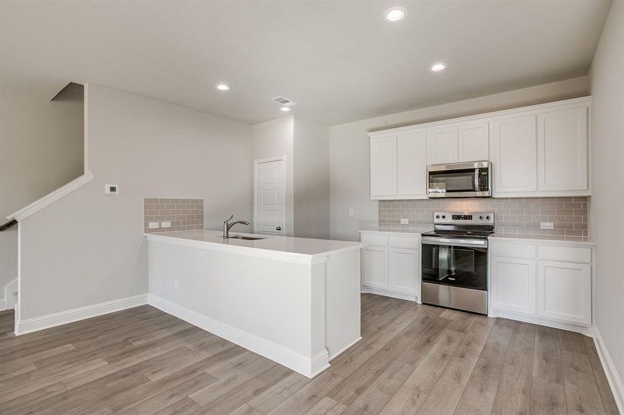 Kitchen with stainless steel appliances, white cabinets, a peninsula, light wood finished floors, and recessed lighting