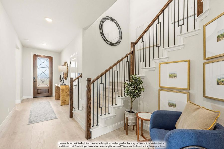 Entryway with staircase featuring wood handrail and iron balusters, hardwood floors, and glass-panel front door