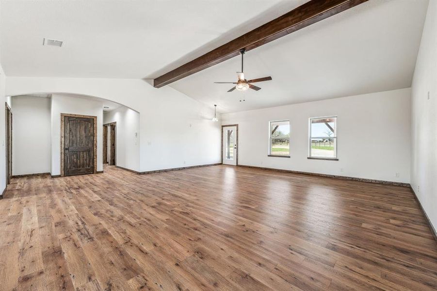 Unfurnished living room featuring lofted ceiling with beams, arched walkways, visible vents, ceiling fan, and wood finished floors