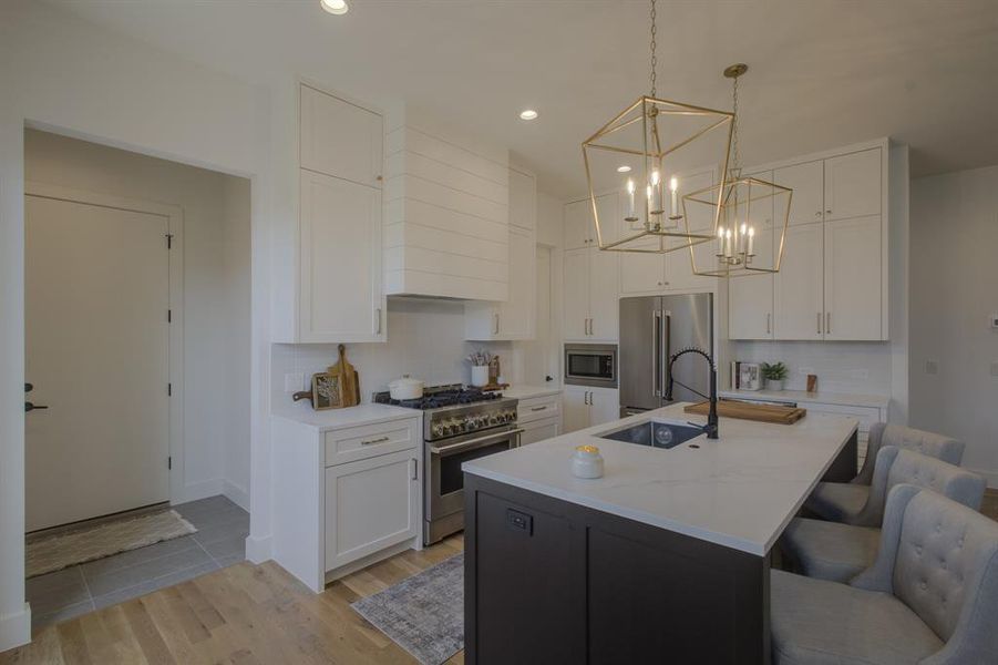 Kitchen with sink, a center island with sink, high quality appliances, white cabinets, and hanging light fixtures