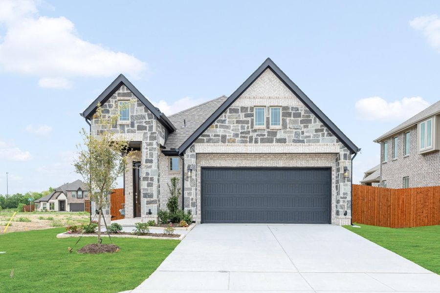 Single-story stone and brick home with two-car garage, concrete driveway, and green front lawn