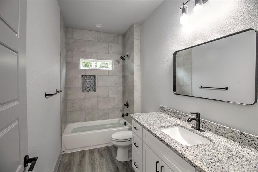 Bathroom with shower combination, vanity, light wood finished floors, and a textured wall Bathroom with shower combination, vanity, light wood finished floors, and a textured wall