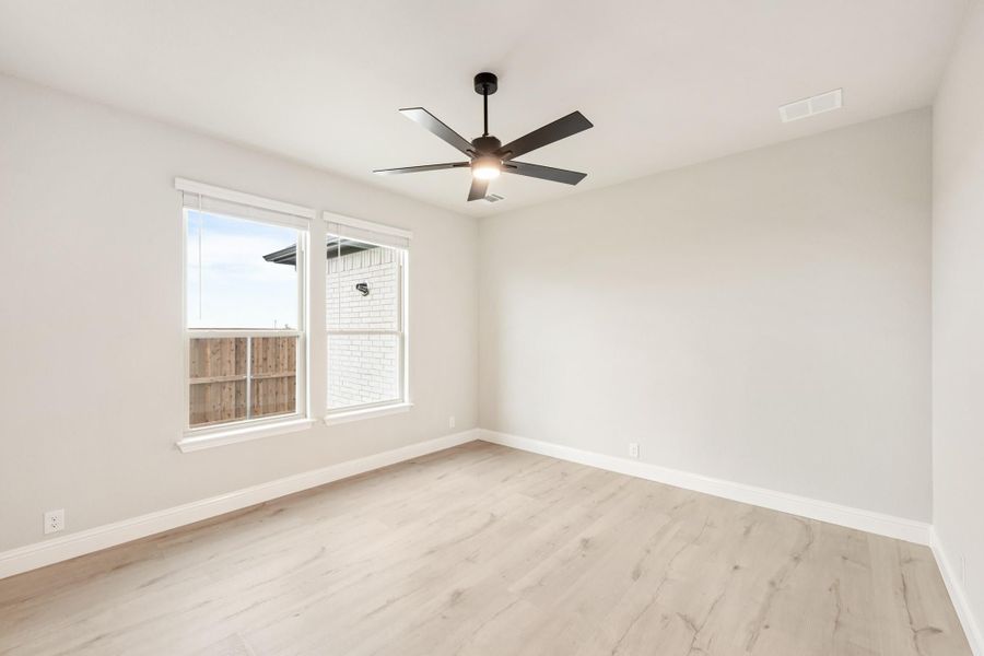Empty bedroom with light wood floors, ceiling fan, and double windows with natural light
