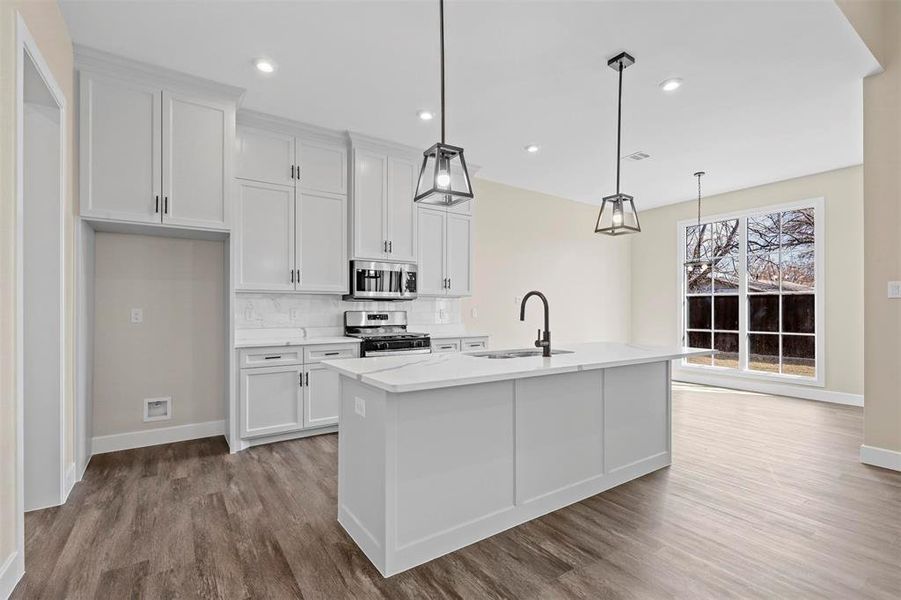 Kitchen featuring appliances with stainless steel finishes, sink, white cabinetry, decorative light fixtures, and an island with sink