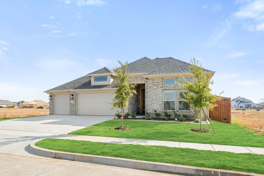 Single-story brick home with two-car garage, green lawn, and young trees in front yard