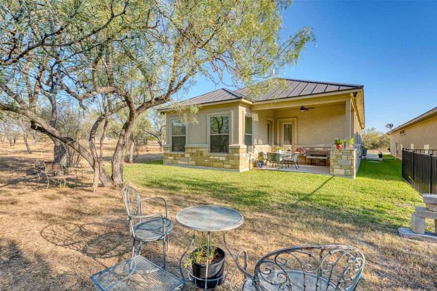 Back of property with ceiling fan, a patio area, a metal roof, a yard, and stone siding