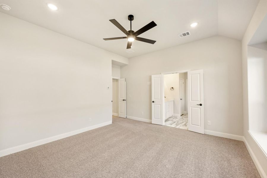 Empty master bedroom with carpet, ceiling fan, and open doors leading to ensuite bathroom