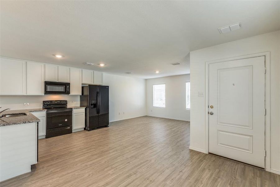 Kitchen featuring light stone counters, sink, black appliances, light hardwood / wood-style flooring, and white cabinets