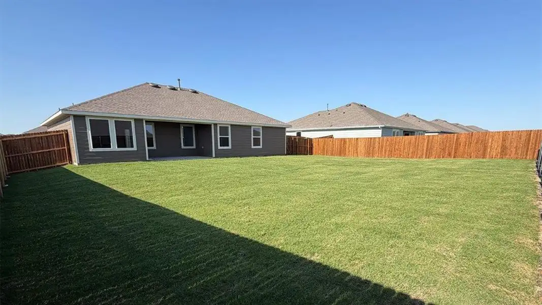 Expansive fenced backyard featuring a manicured lawn, a charcoal gray exterior with white trim, a covered patio, and multiple windows