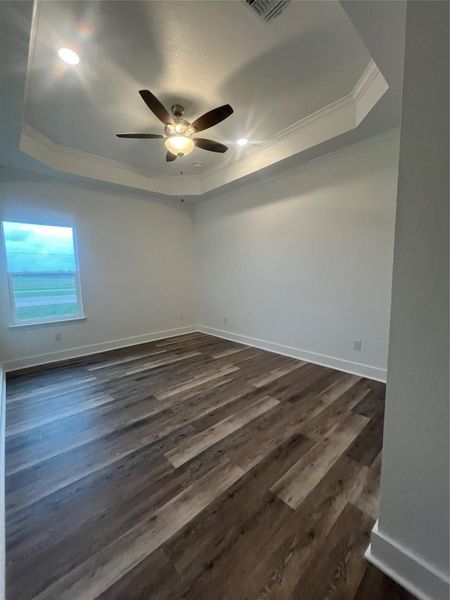 This room features elegant medium gray/wood water proof flooring, a tray ceiling with recessed lighting, and a ceiling fan. A large window allows for natural light, creating a bright and inviting space.