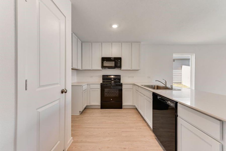 Kitchen featuring light wood-style flooring, light countertops, black appliances, white cabinetry, and a sink