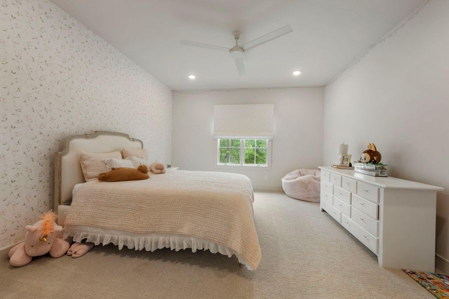 Elegant secondary bedroom featuring soft carpeting, recessed lighting, designer wallpaper accent wall, and a large window that fills the space with natural light.