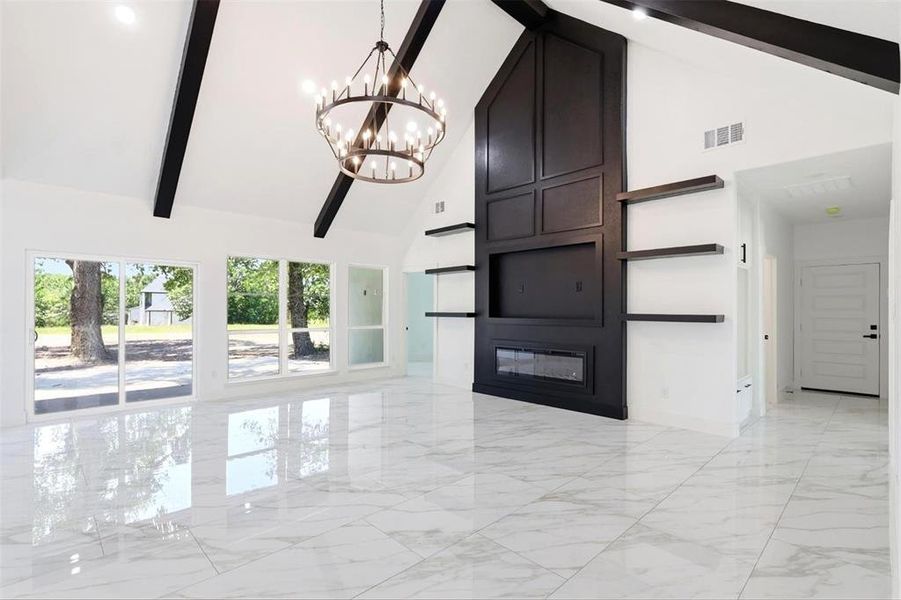 Great room featuring a vaulted ceiling with exposed dark beams, a large decorative chandelier, and white marble-look tile flooring