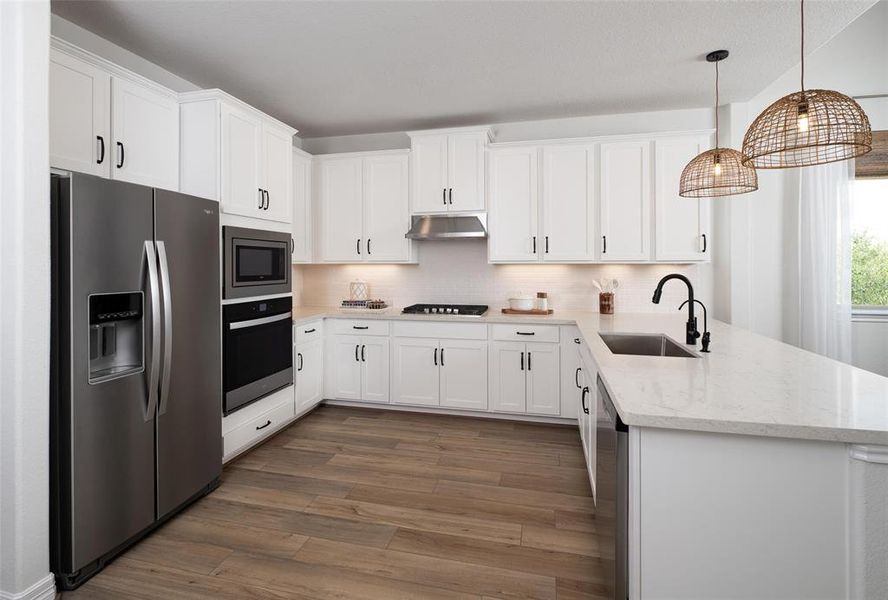 This light and bright kitchen features a large quartz island, white cabinets, a large sink overlooking your family room, recessed lighting, and beautiful backsplash.