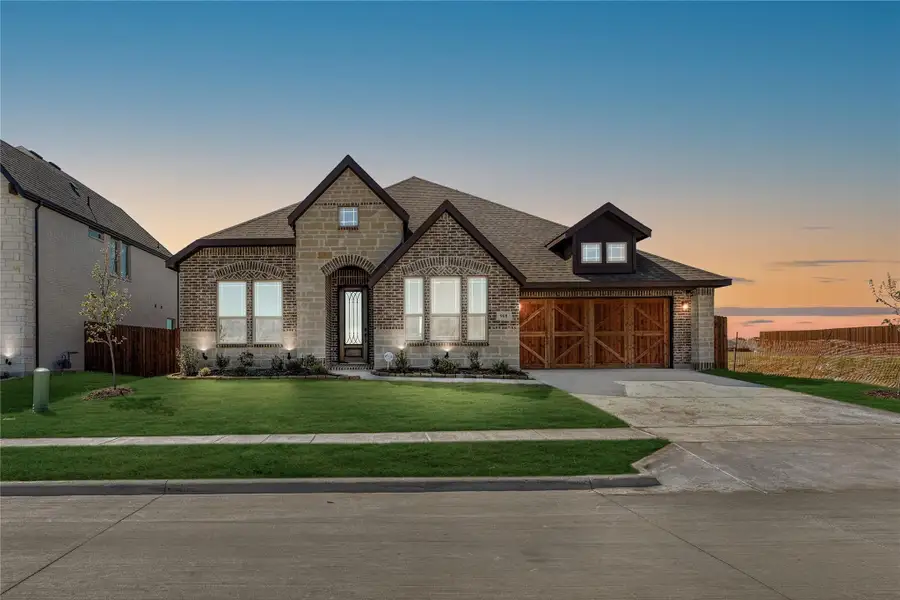 Single-story home with brick and stone exterior, two-car garage with wood doors, and green front lawn at dusk Single-story home with brick and stone exterior, two-car garage with wood doors, and green front lawn at dusk