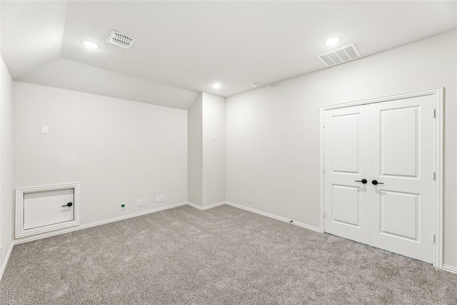 Empty bedroom with gray carpet, white walls, double closet doors, and a small wall access panel