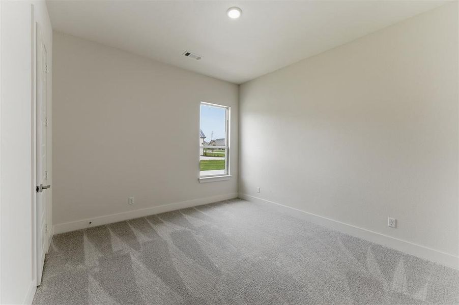 Bright interior space featuring light-toned walls, grey patterned carpeting, a single pane window, a white door with a metal handle, and a recessed ceiling light fixture