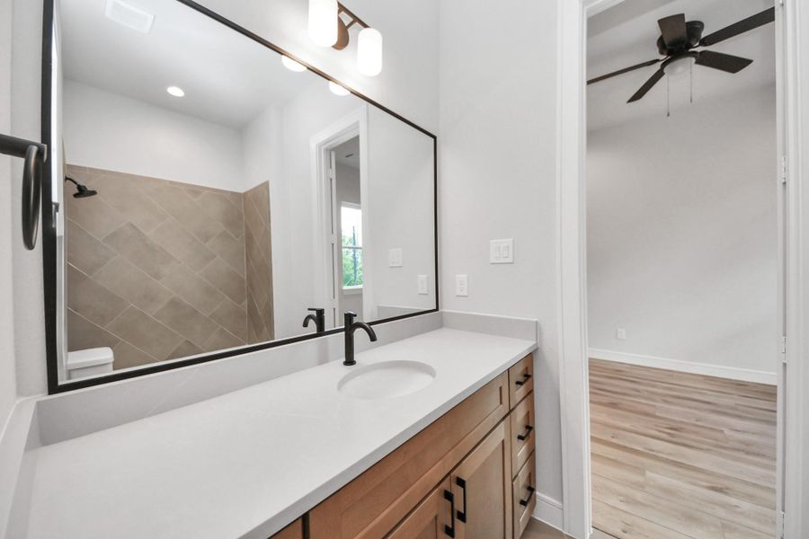 Well-appointed secondary bathroom featuring a framed mirror, upgraded cabinetry with light countertops, and sleek modern finishes that mirror the style and quality of the primary bath.