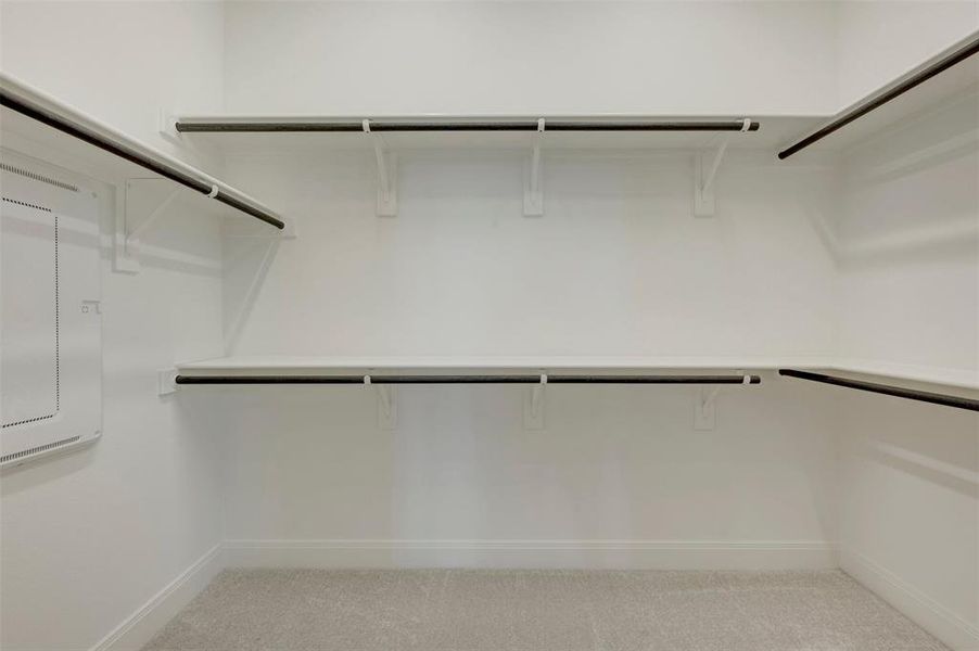 Spacious walk-in closet featuring white painted shelving and dark-finish hanging rods Spacious walk-in closet featuring white painted shelving and dark-finish hanging rods