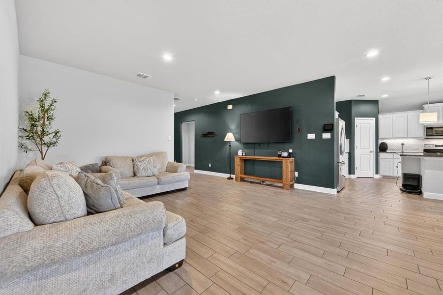 Open-concept living area with wood-finish flooring, recessed lighting, a statement wall, and a partial wall separating spaces