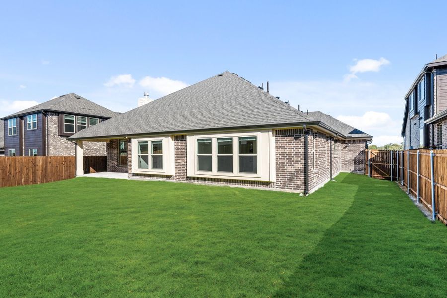 Rear view of brick home with large windows, green lawn, and wood privacy fence Rear view of brick home with large windows, green lawn, and wood privacy fence