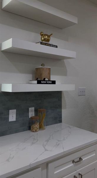White floating shelves above a countertop featuring white cabinetry with silver-tone hardware, a white countertop with gray veining, and a gray subway tile backsplash