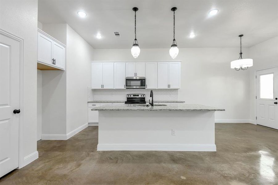 Kitchen featuring concrete floors, a kitchen island with sink, hanging light fixtures, white cabinetry, and recessed lighting