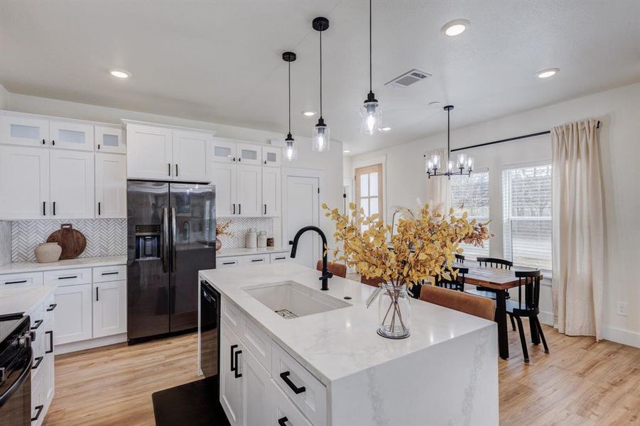 Kitchen with pendant lighting, sink, a kitchen island with sink, backsplash, and stainless steel fridge with ice dispenser Kitchen with pendant lighting, sink, a kitchen island with sink, backsplash, and stainless steel fridge with ice dispenser