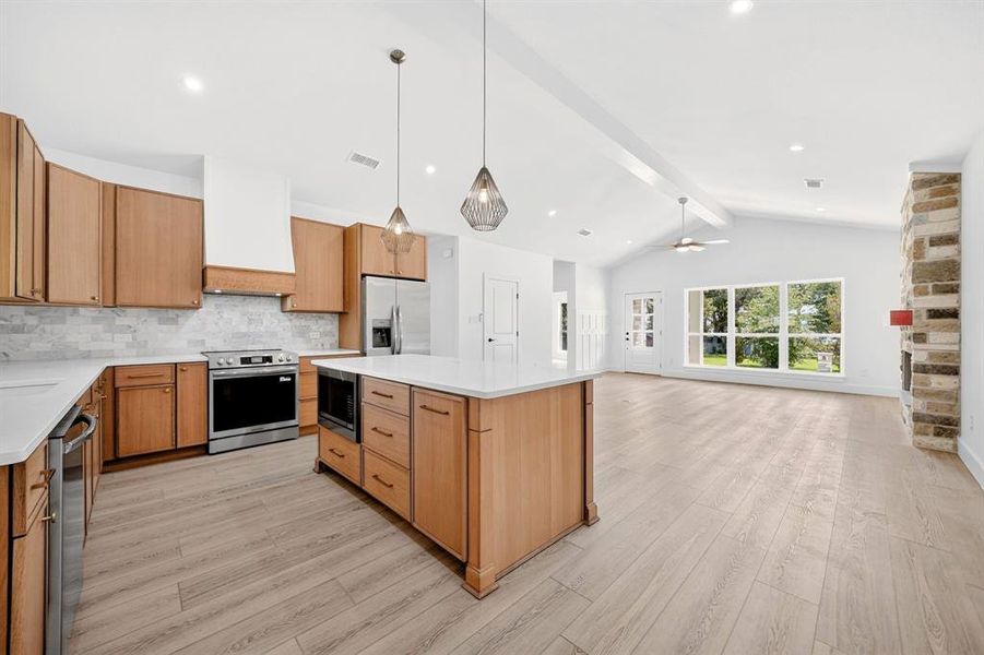 Open-concept kitchen and living area featuring wood-finish flooring, vaulted ceilings, and recessed lighting