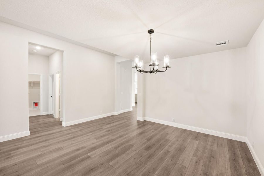Empty dining room with gray hardwood floors, white walls, and a black chandelier overhead.