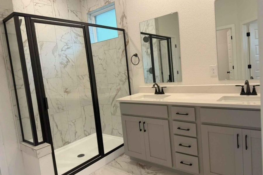 Bathroom featuring double vanity, a marble finish shower, and light marble finish flooring