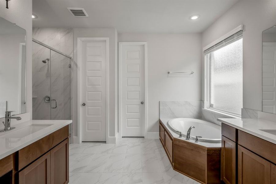 You'll love getting ready in this light and bright primary bathroom! The primary bathroom includes two separate vanities, warm wood cabinets, quartz countertops, marbled flooring, large garden tub, and walk-in shower.