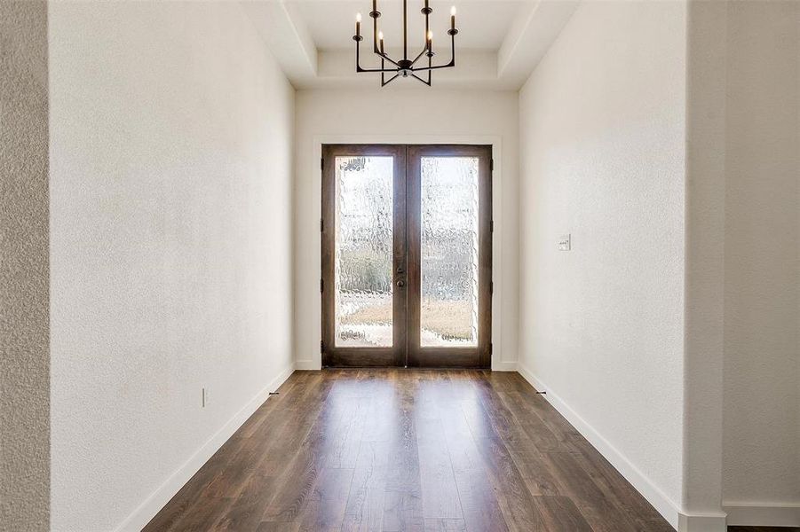 Entryway with french doors, an inviting chandelier, a tray ceiling, and dark wood-type flooring