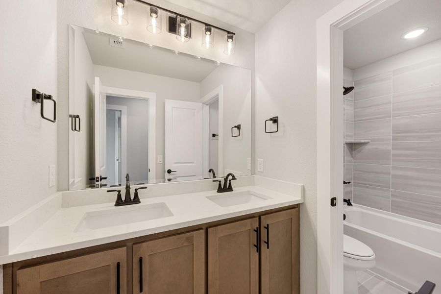 Bathroom with double sink vanity, wood cabinets, white countertop, large mirror, and tiled shower-tub combo Bathroom with double sink vanity, wood cabinets, white countertop, large mirror, and tiled shower-tub combo