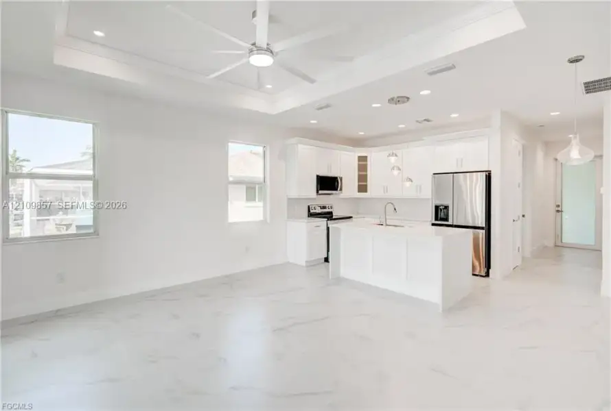 Kitchen featuring white cabinetry, an island with stone-finish countertops, recessed lighting, a tray ceiling with a center fan, and polished tile flooring