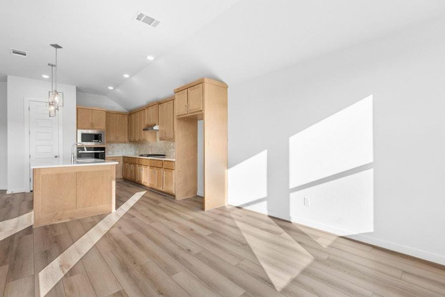 Kitchen featuring vaulted ceiling, light brown cabinets, light countertops, tasteful backsplash, and pendant lighting