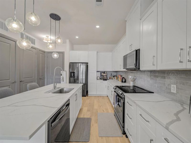 Kitchen featuring stainless steel appliances, white cabinetry, decorative light fixtures, light stone countertops, and light wood-style floors Kitchen featuring stainless steel appliances, white cabinetry, decorative light fixtures, light stone countertops, and light wood-style floors