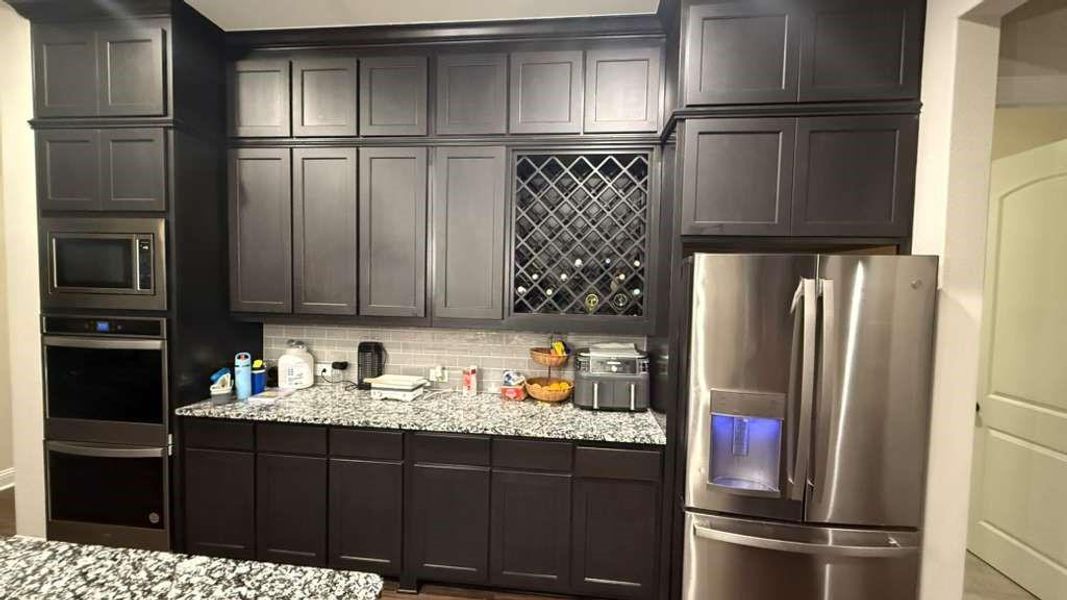 Kitchen featuring appliances with stainless steel finishes, decorative backsplash, and light stone counters