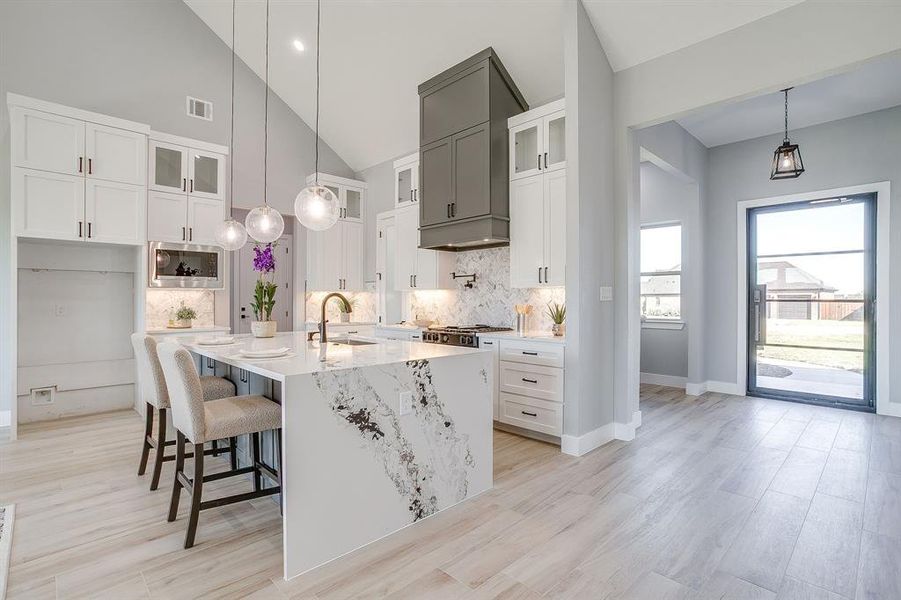 Kitchen with glass insert cabinets, a breakfast bar, light stone counters, pendant lighting, and white cabinets