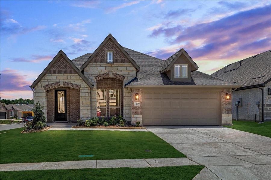 Single-story home with brick and stone exterior, arched entry, two-car garage, and green front lawn at dusk Single-story home with brick and stone exterior, arched entry, two-car garage, and green front lawn at dusk