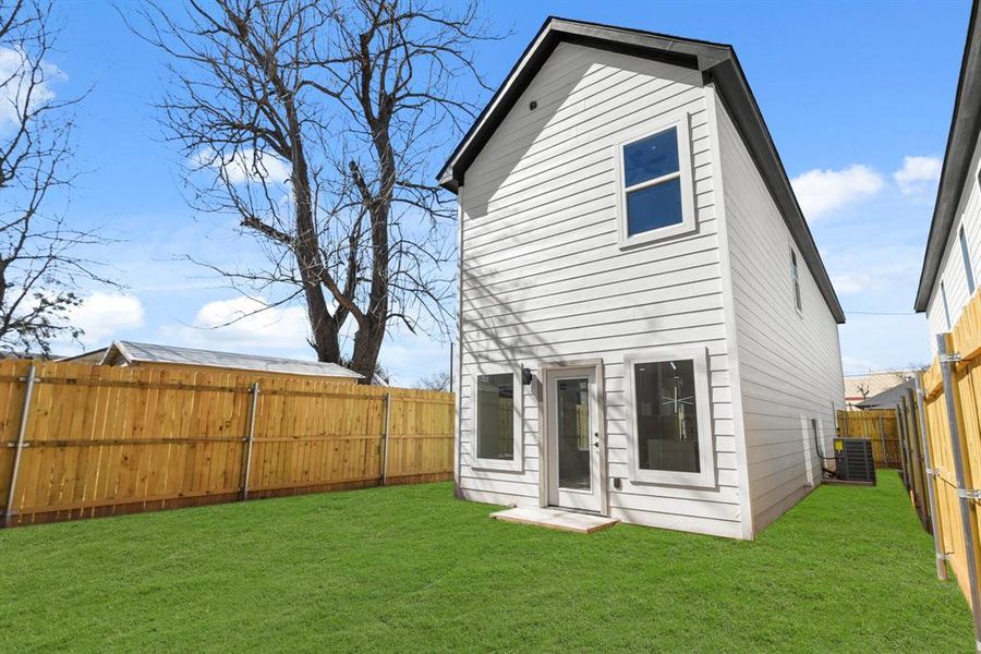 Rear view of house featuring a fenced backyard, central AC, and a lawn