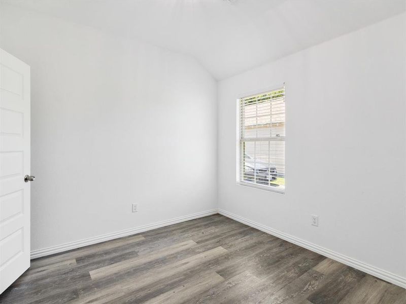Room featuring wood-finish flooring, white baseboards, a white paneled door with a silver knob, and a window with white horizontal blinds