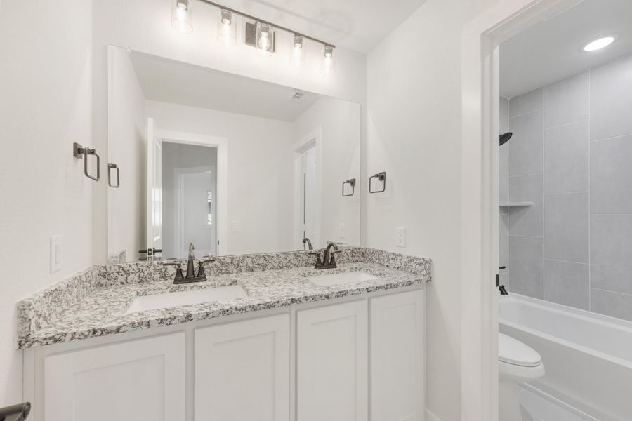 Bathroom with double vanity, granite countertops, white cabinets, and tiled shower-tub combo