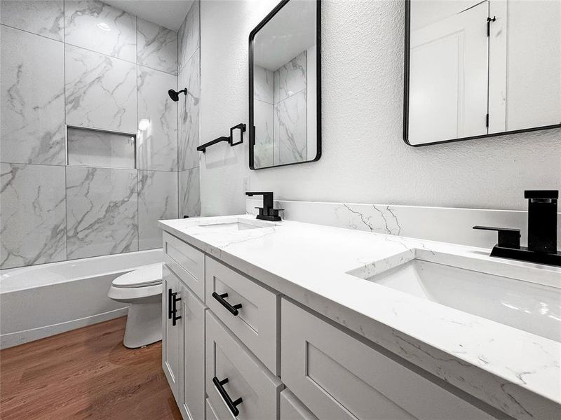 Full bath with toilet, double vanity, wood finished floors, and shower / bath combination