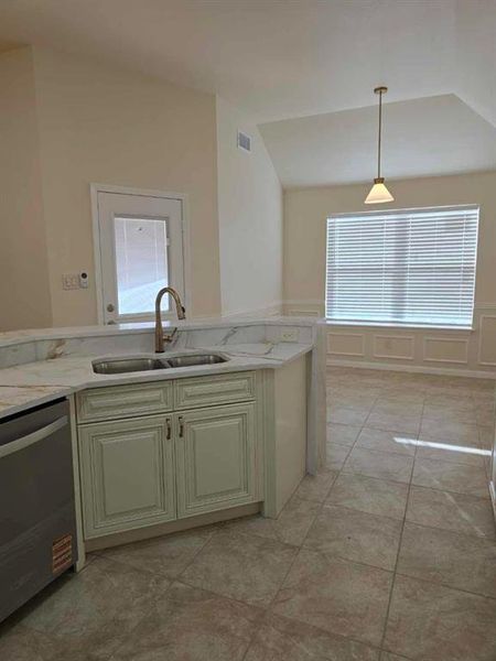 Kitchen with decorative light fixtures, stainless steel dishwasher, light stone counters, wainscoting, and cream cabinetry Kitchen with decorative light fixtures, stainless steel dishwasher, light stone counters, wainscoting, and cream cabinetry